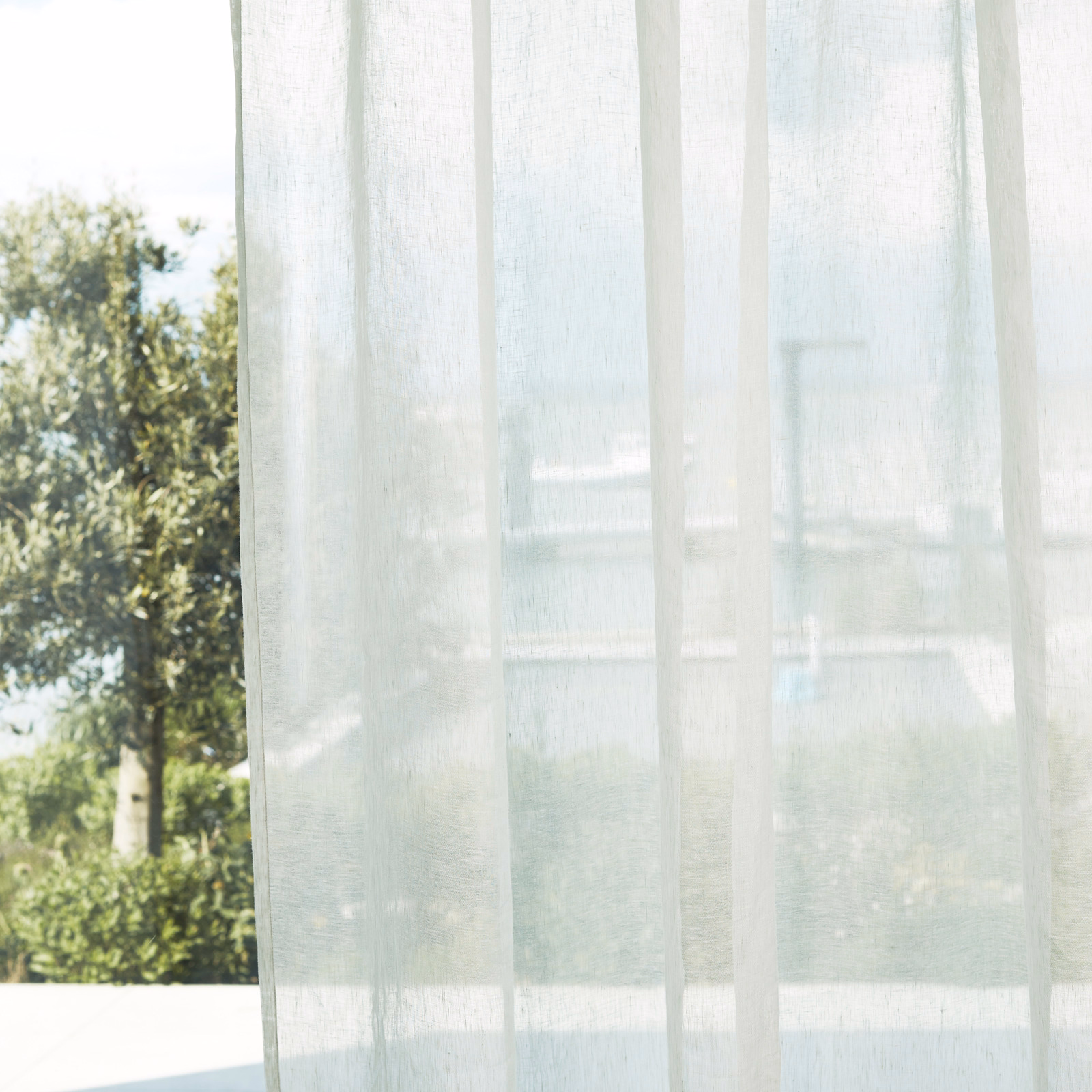 Pale oyster sheer curtain with subtle vertical bands, diffusing a leafy outdoor view