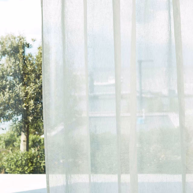 Pale oyster sheer curtain with subtle vertical bands, diffusing a leafy outdoor view