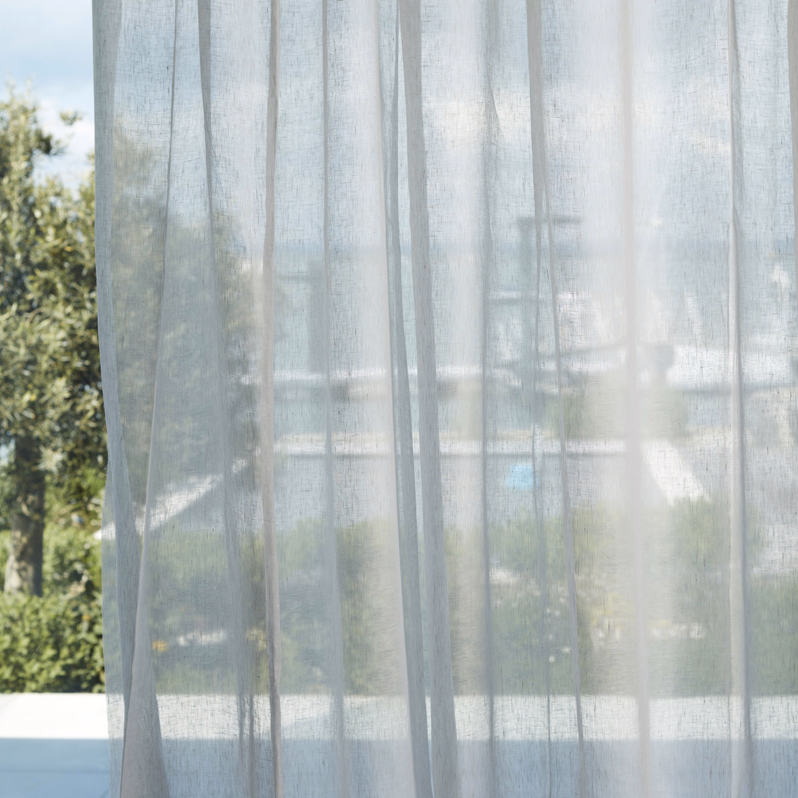 Pale blue-grey sheer with fine vertical weave filtering daylight across a window