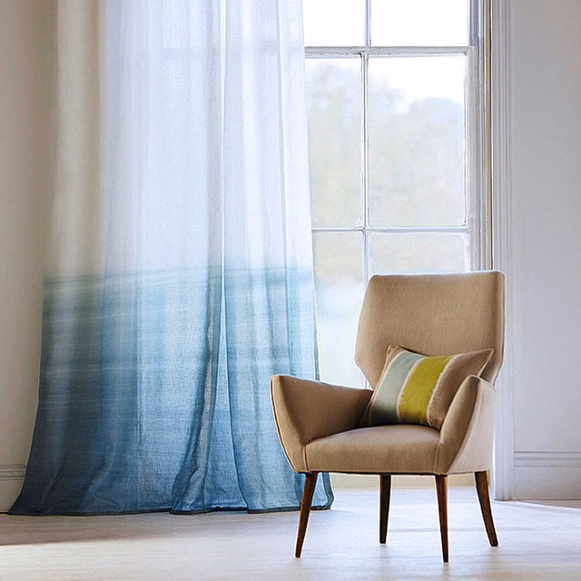 Translucent chalk-to-sky-blue ombré sheer curtain glowing beside a window