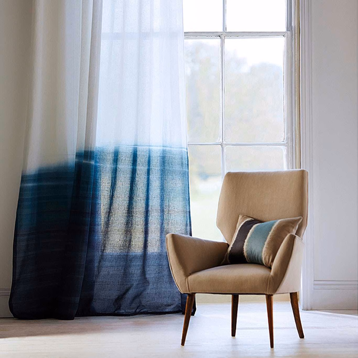 Sheer curtain fading from pale aqua to deep slate blue beside a sunlit window