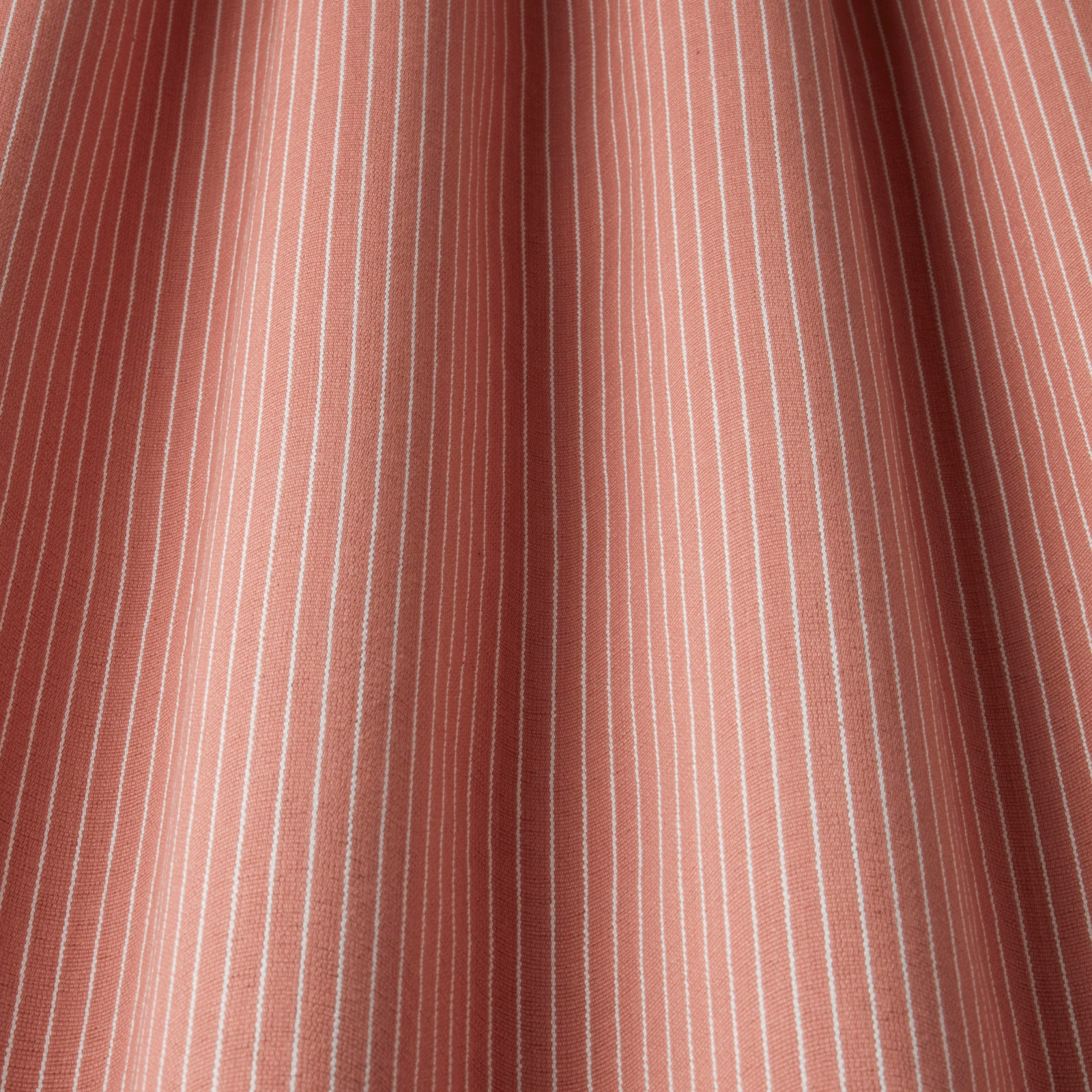 Raspberry pink cotton fabric with fine vertical white pinstripes and soft folds