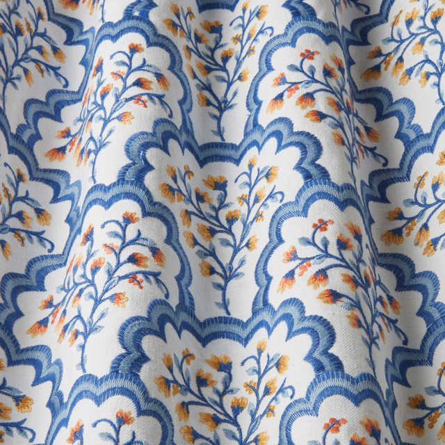 Blue scalloped floral fabric with orange embroidered sprigs on an off-white ground