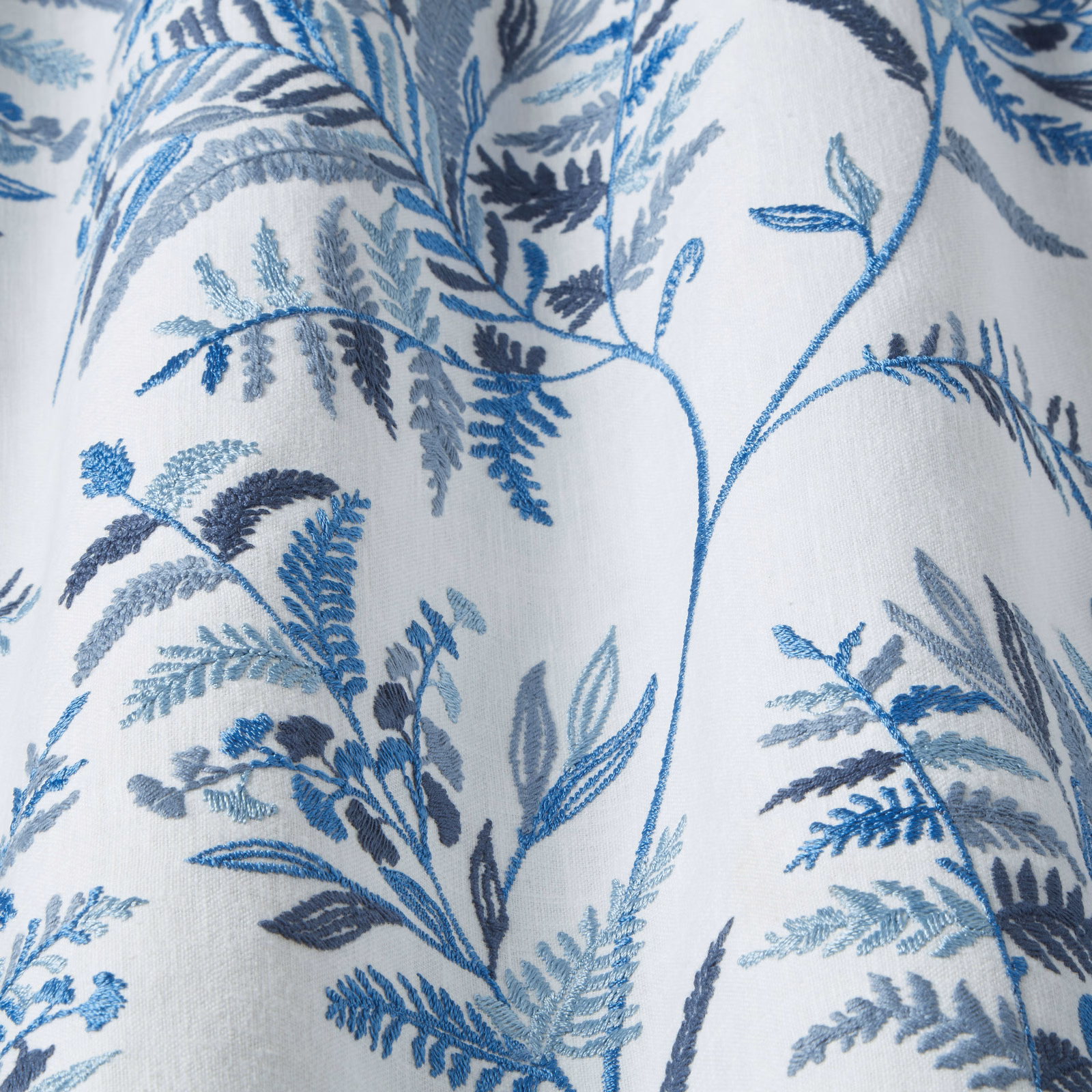 Blue and grey botanical embroidered fabric on a pale ground