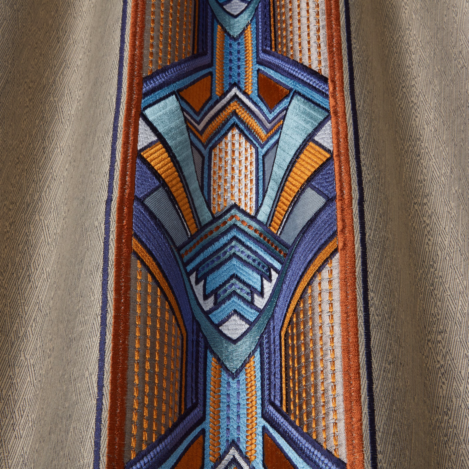 Close-up of geometric woven fabric in navy, teal, aqua and orange with a textured sheen