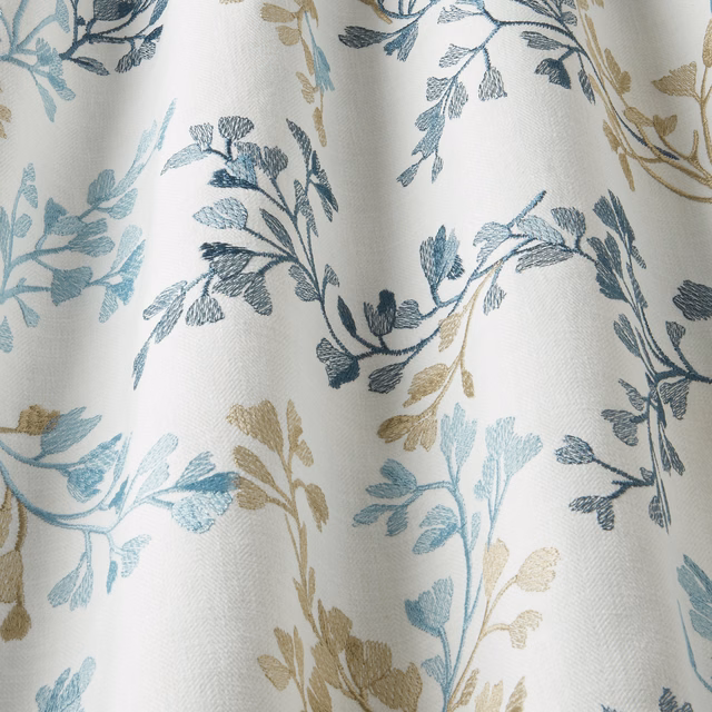 Pale cotton fabric with wavy blue and taupe leaf branches on an ivory ground