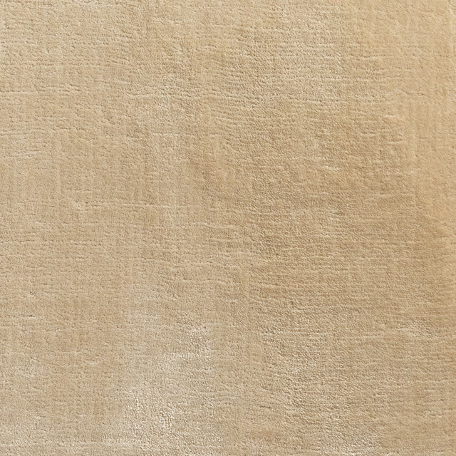Warm wheat-beige carpet swatch with fine mottled texture and softly uneven shading