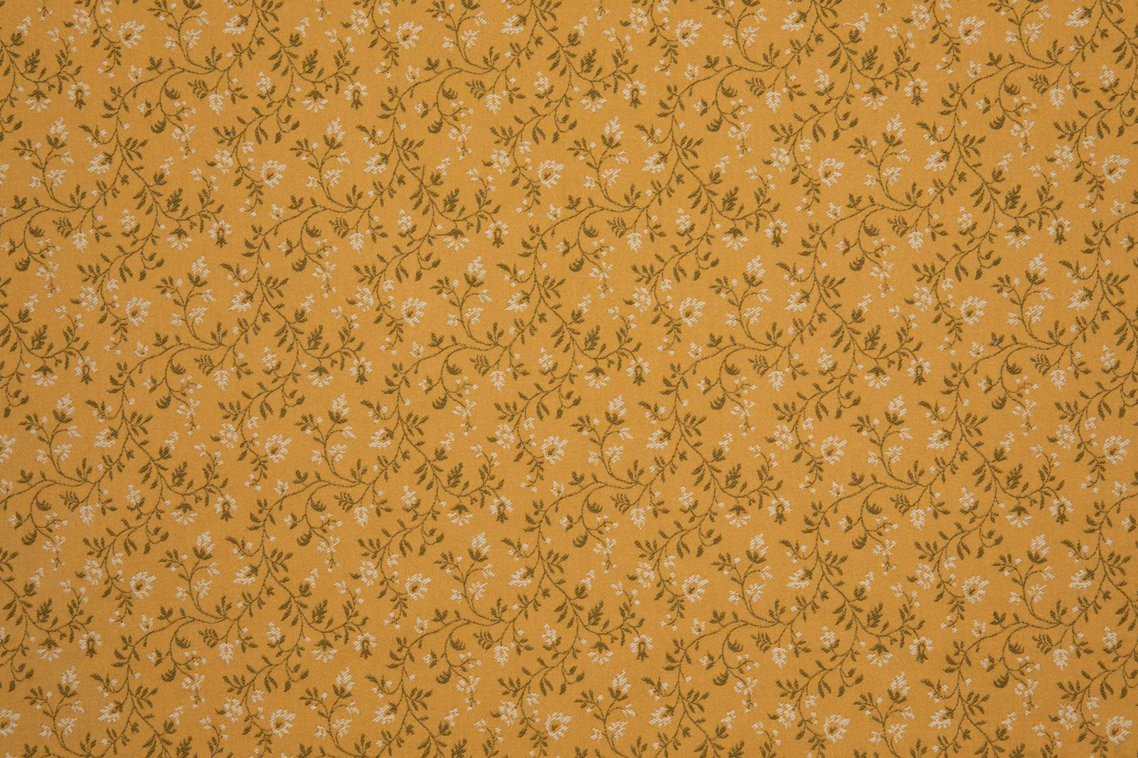 Warm ochre-gold textile with small pale blossoms and curling dark stems