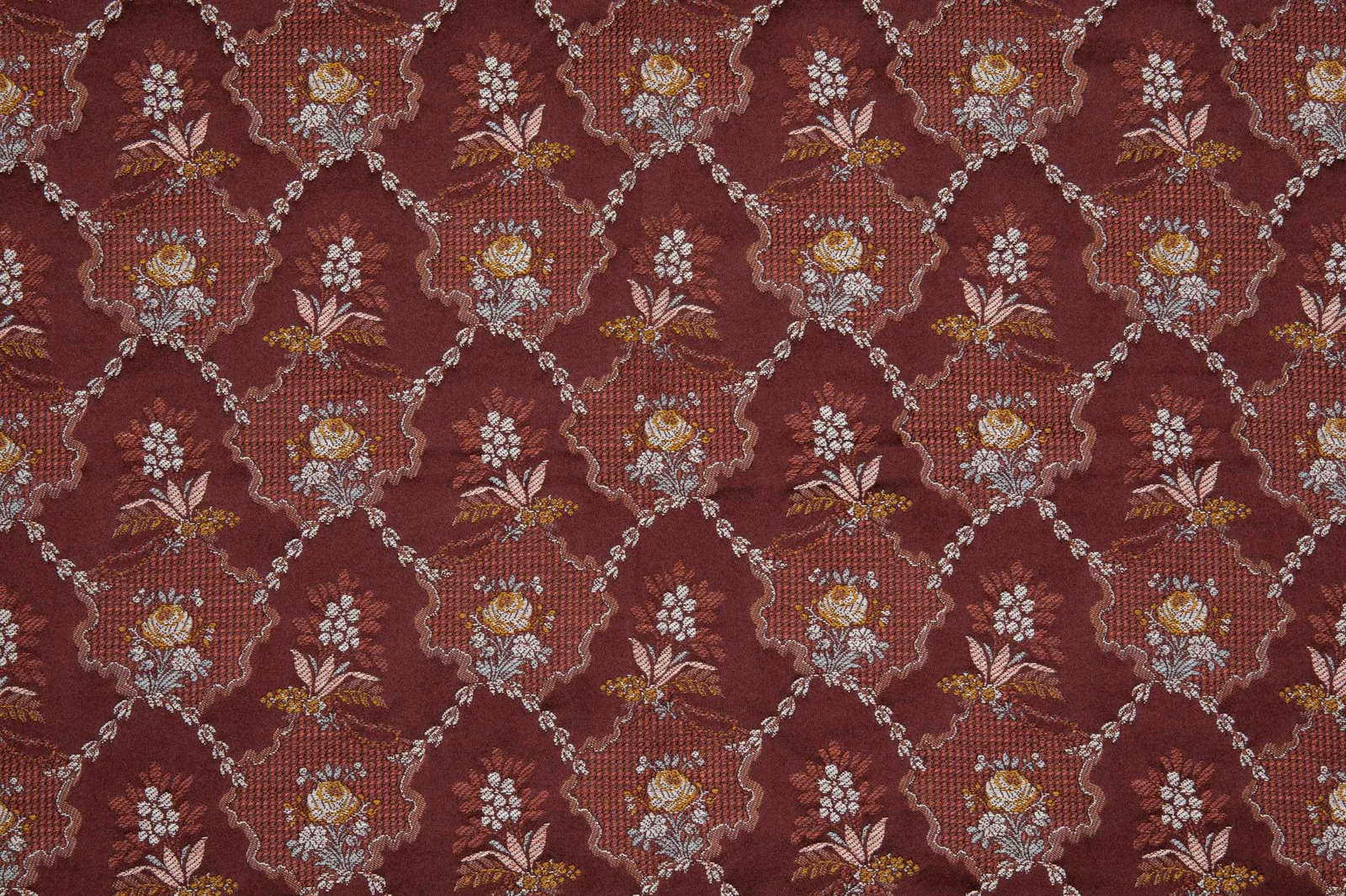 Deep garnet woven fabric with cream and gold floral bouquets in a scrolling lattice