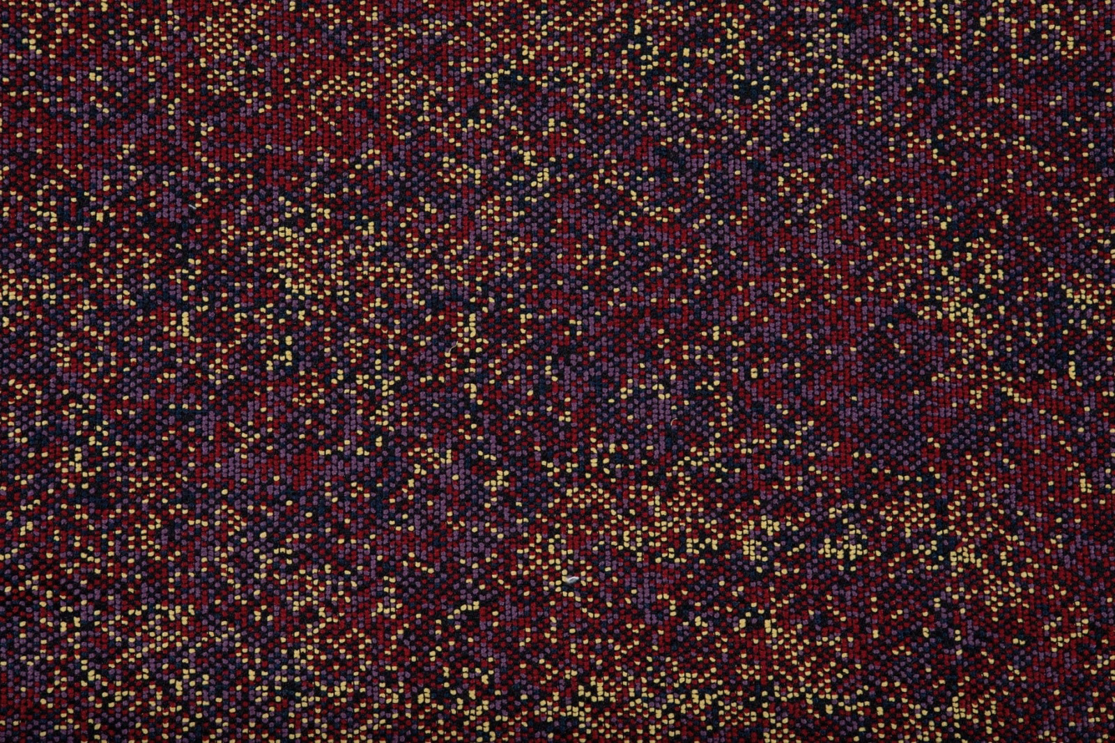 Dark fig-plum textile with burgundy depth and scattered ochre, teal, and gold flecks