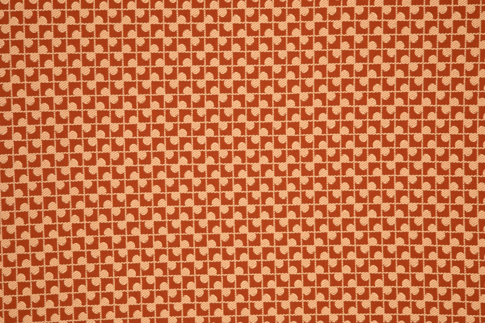 Warm brick-red fabric with cream interlocking geometric motifs and a lightly textured weave