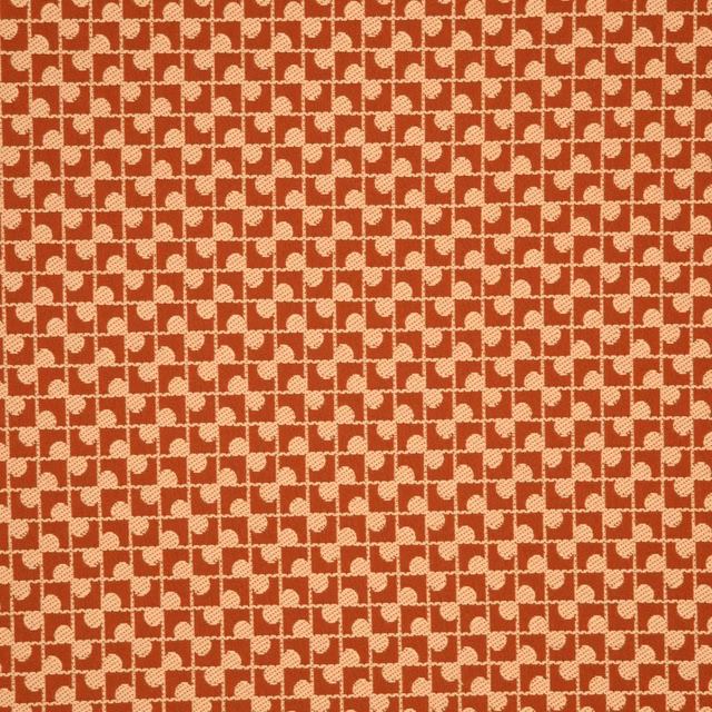 Warm brick-red fabric with cream interlocking geometric motifs and a lightly textured weave