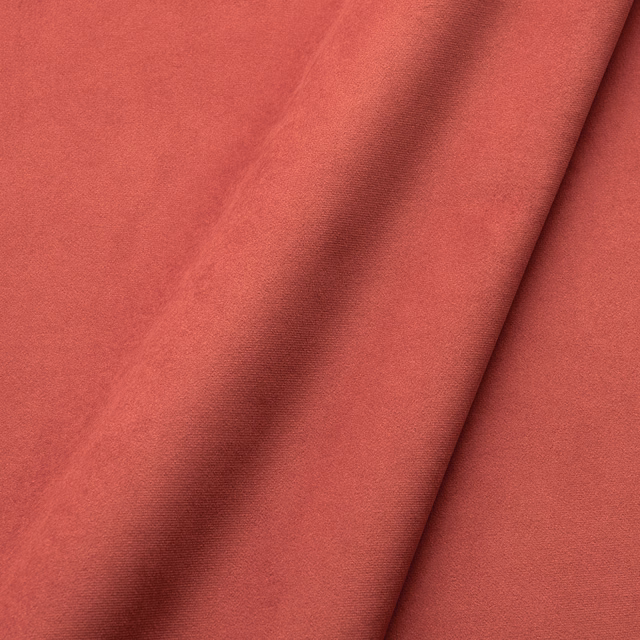 Warm coral-red velvet showing soft directional pile and deep shadows in folded fabric