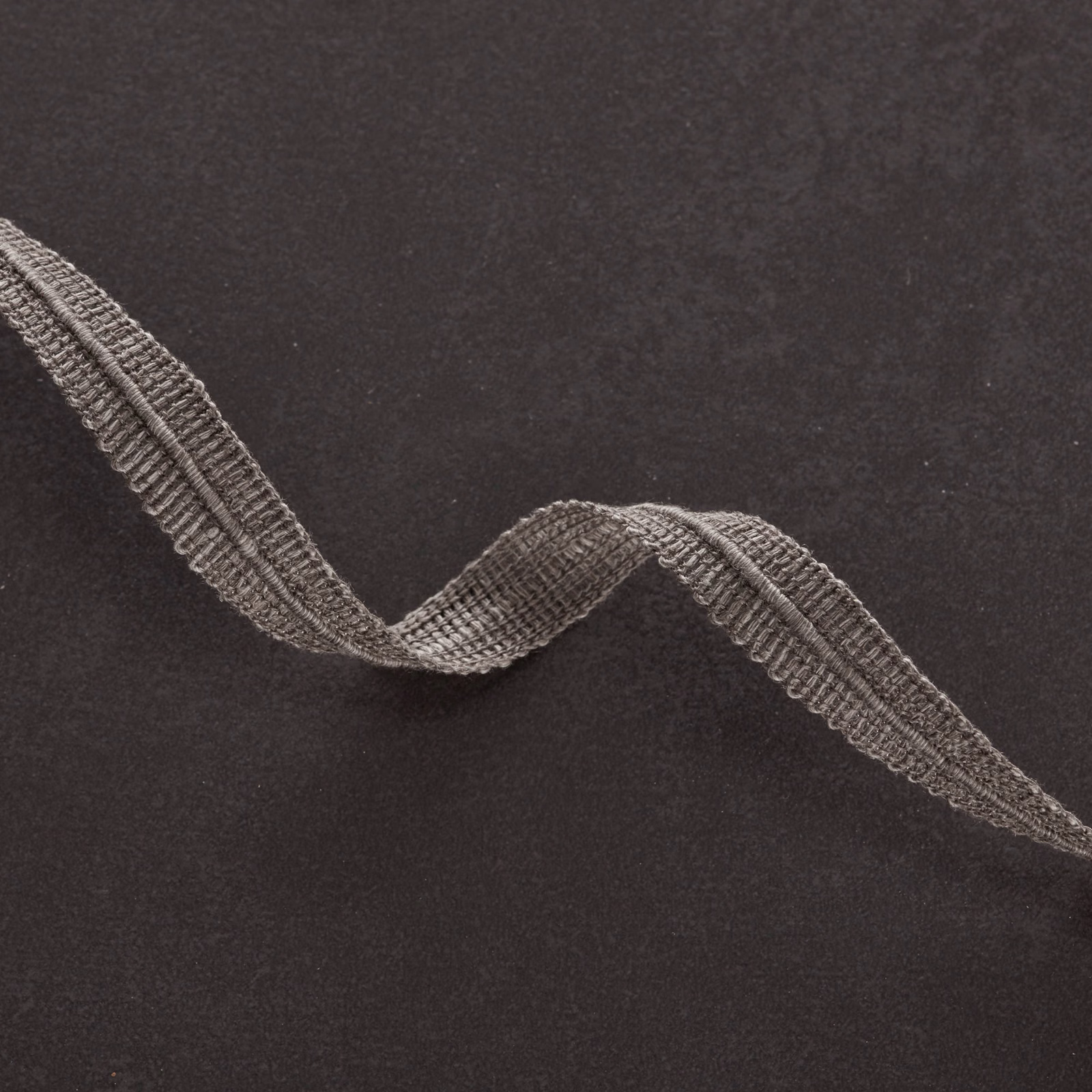 Dark gunmetal textile with a raised, looping grey wave across its matte surface