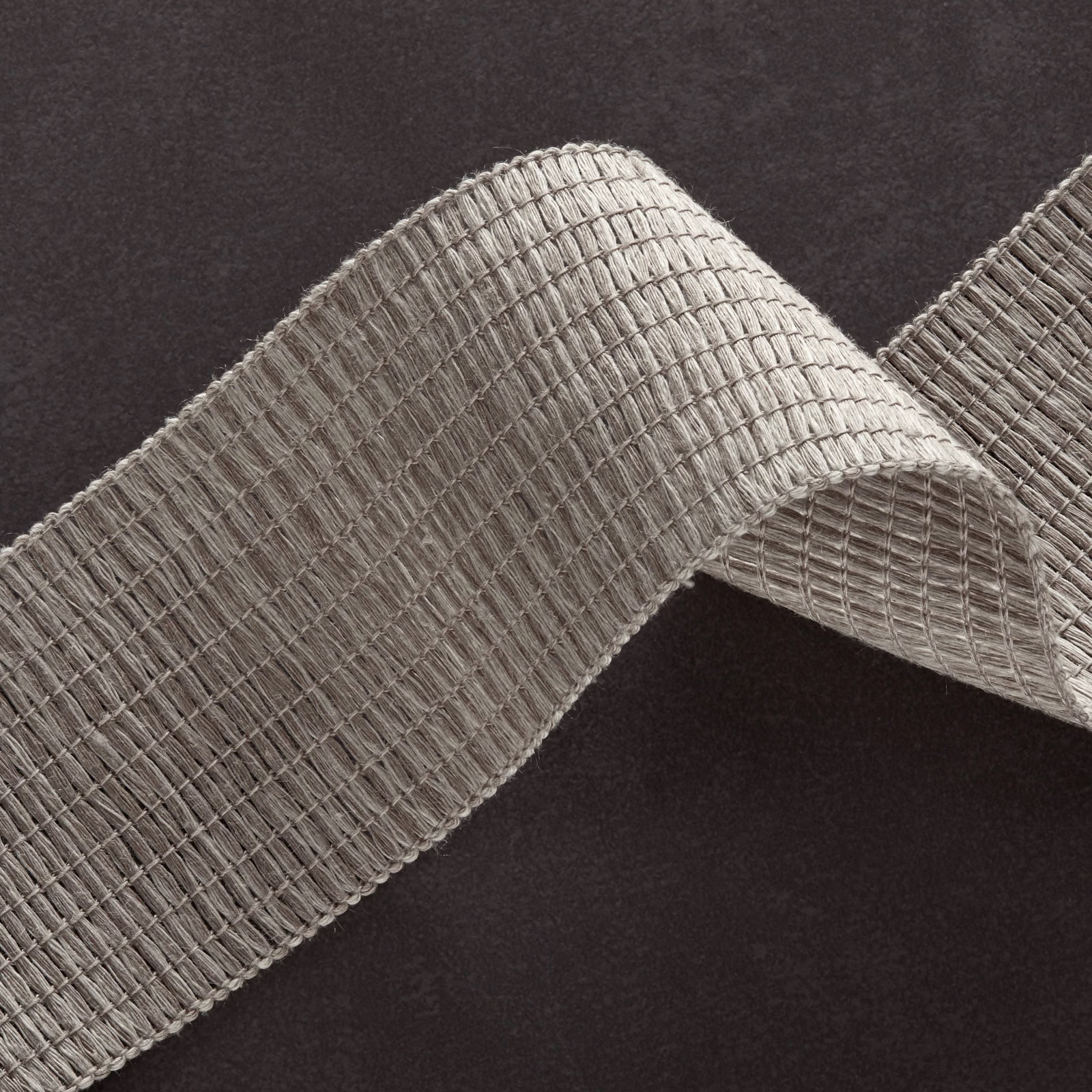 Cool cement-grey ribbed weave folded into a sculptural loop on dark ground