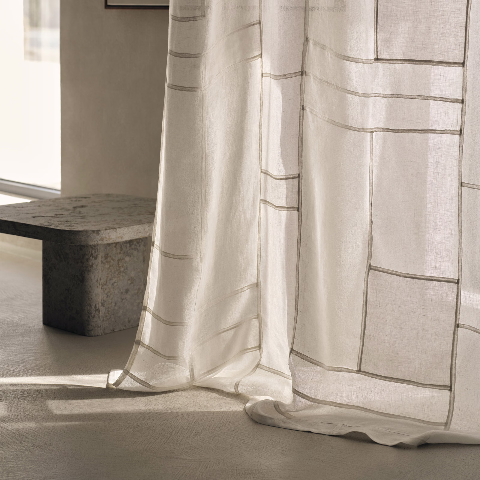 Sheer ivory curtain with taupe rectangular embroidery glowing in soft daylight