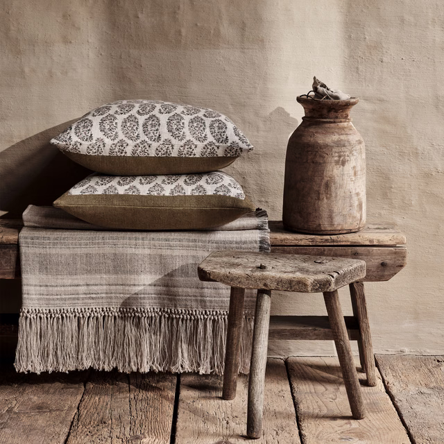 Warm cumin-beige textile with repeating brown botanical medallions on two cushions