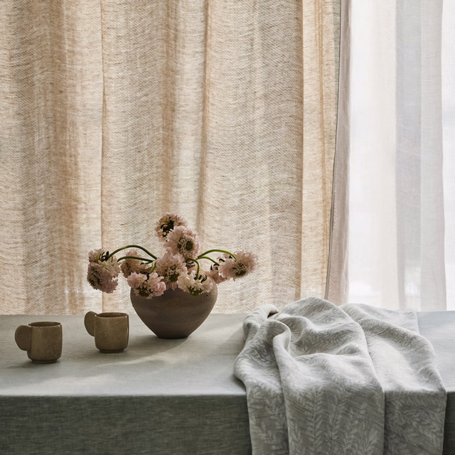 Pale stone grey-beige fabric with subtle feathery woven texture draped over a table