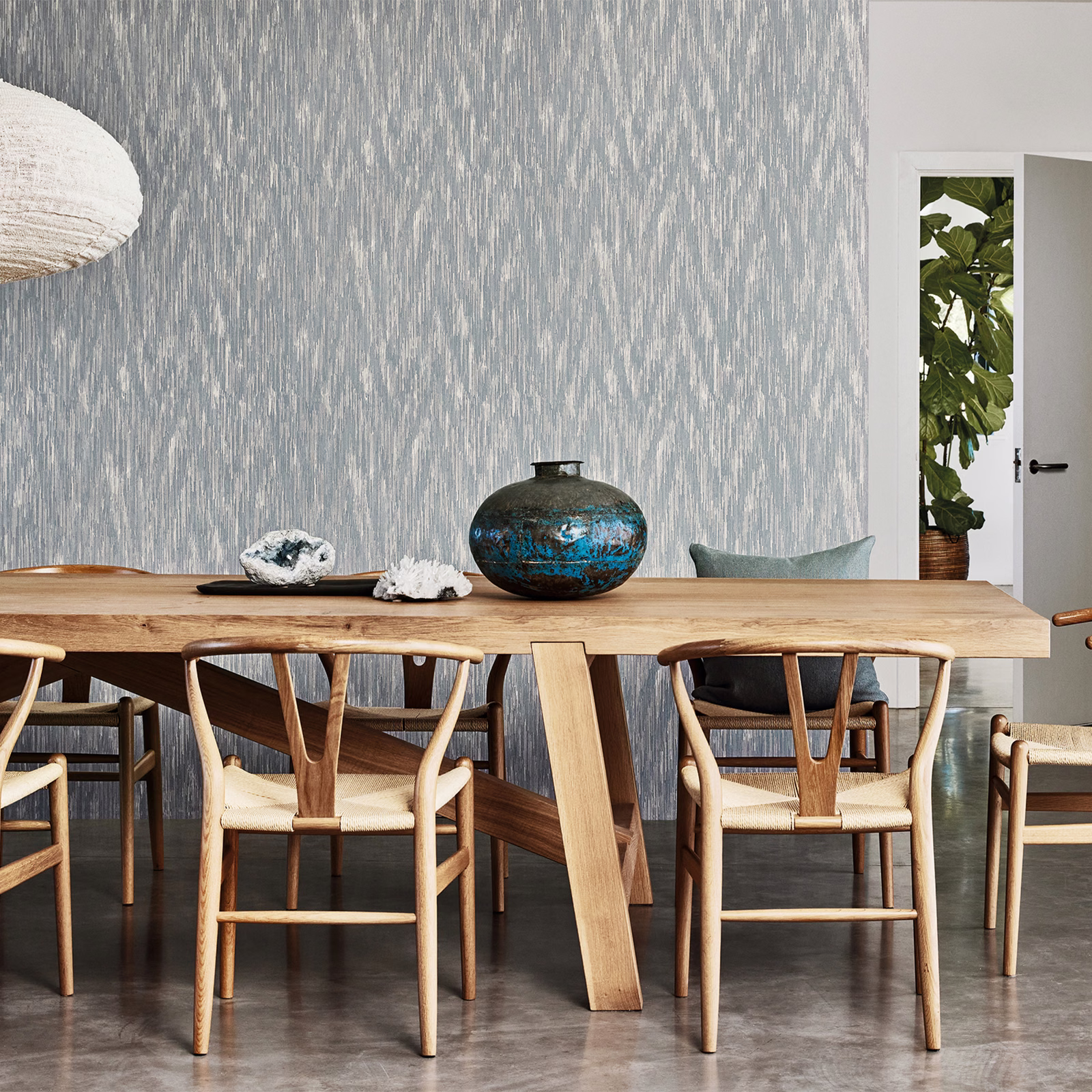 Silver-blue wallpaper with fine broken vertical striations behind a warm timber dining table