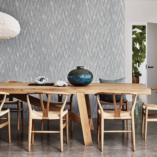 Silver-blue wallpaper with fine broken vertical striations behind a warm timber dining table