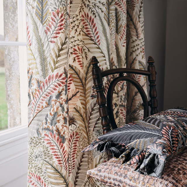 Warm ivory curtain with coral, sage and blue-grey fern foliage beside a dark wooden chair