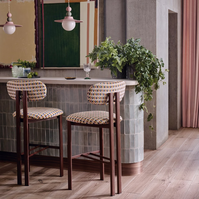 Cream woven upholstery with tiny teal, pink, ochre and dark geometric motifs on bar stools
