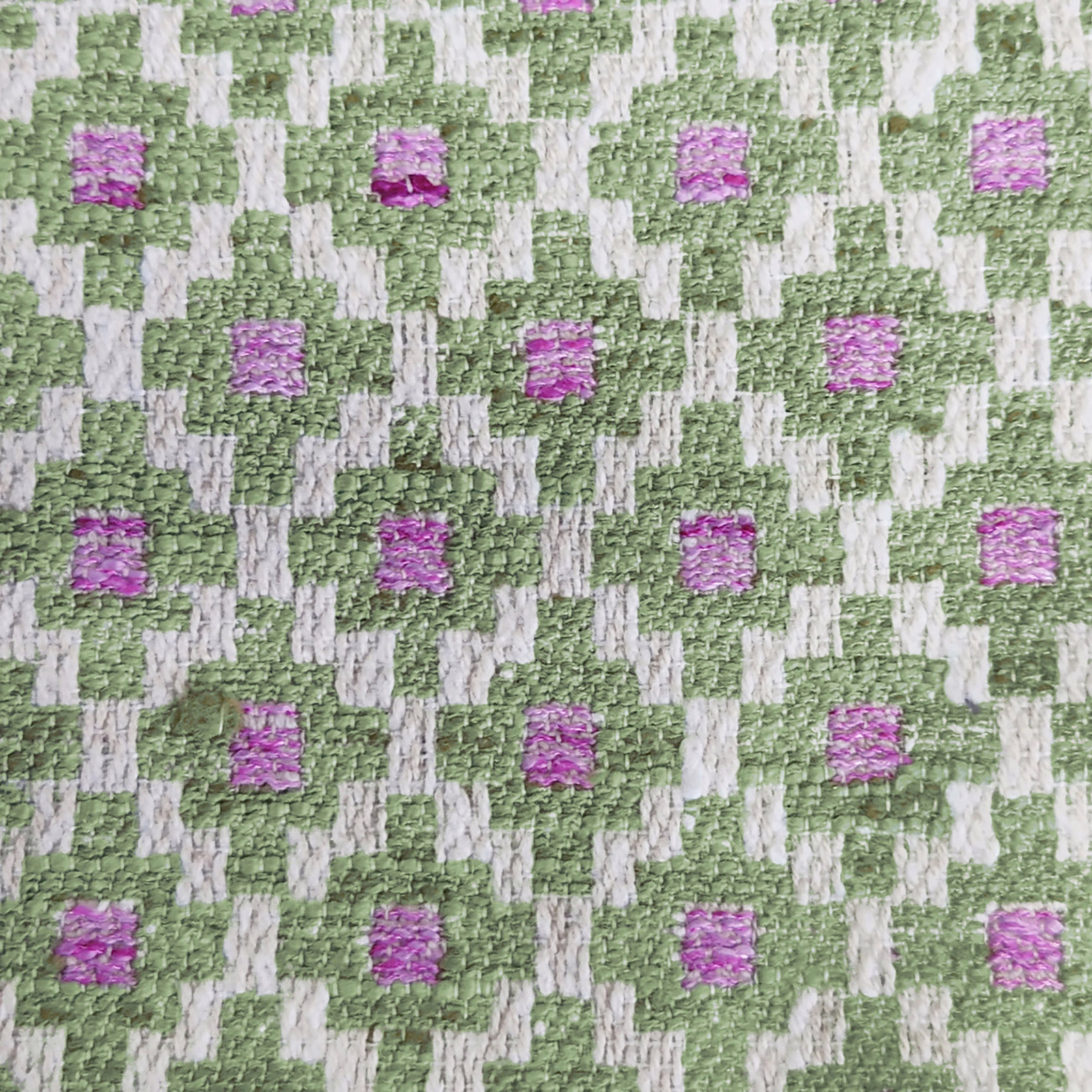 Close-up of a green and ivory geometric woven fabric with pink square accents