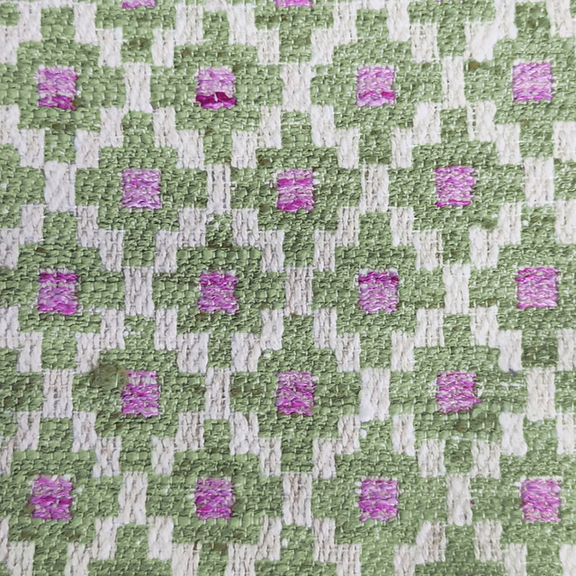 Close-up of a green and ivory geometric woven fabric with pink square accents