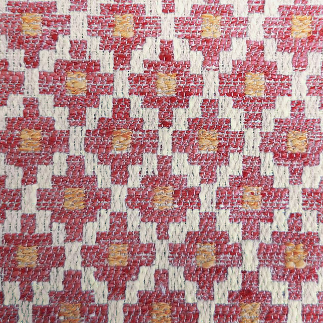 Close-up of coral-orange geometric woven fabric with cream lattice and ochre flecks