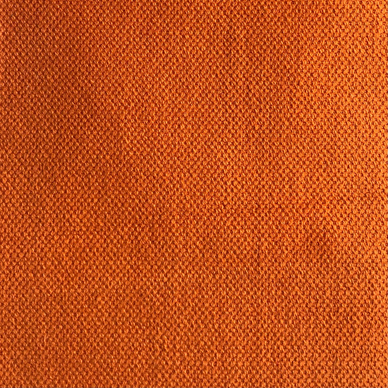 Close-up of saturated terracotta-orange fabric with fine diagonal woven texture and darker flecks