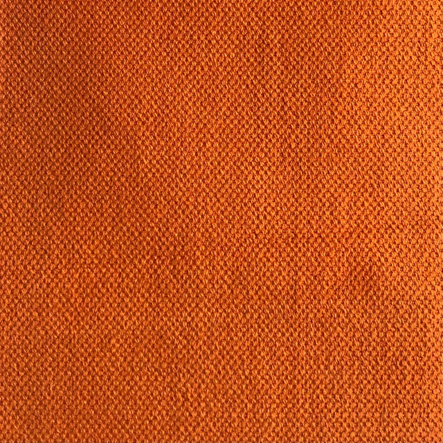 Close-up of saturated terracotta-orange fabric with fine diagonal woven texture and darker flecks