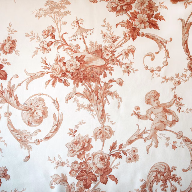 Blush rose toile fabric with scrolling florals and cherub motifs on a pale ground