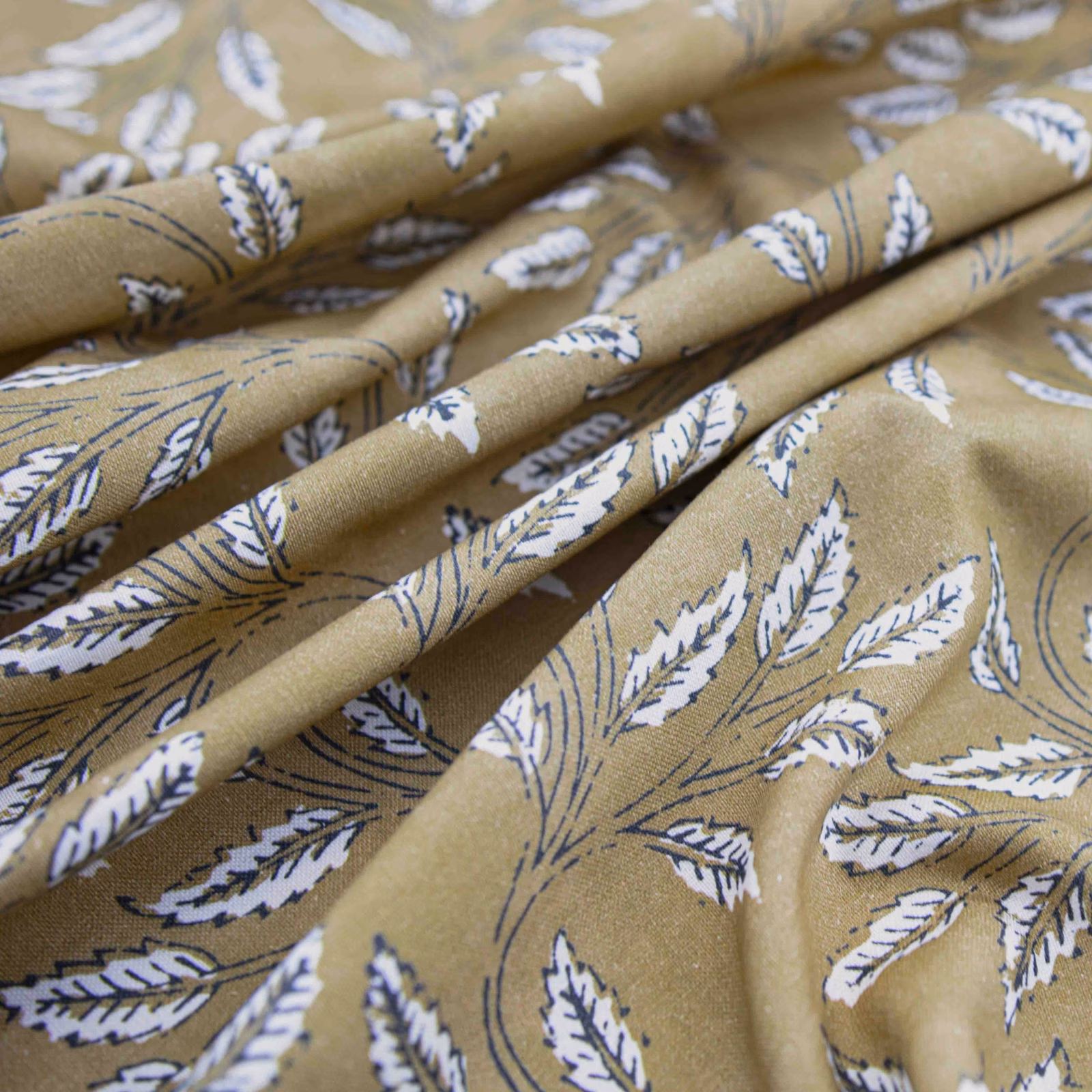 Warm saffron-ochre fabric with white leaf sprigs and navy outlines in soft folds
