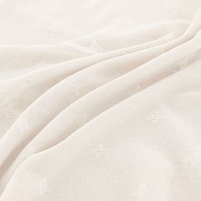 Warm ivory woven fabric with tiny tonal bee motifs and soft fluid folds