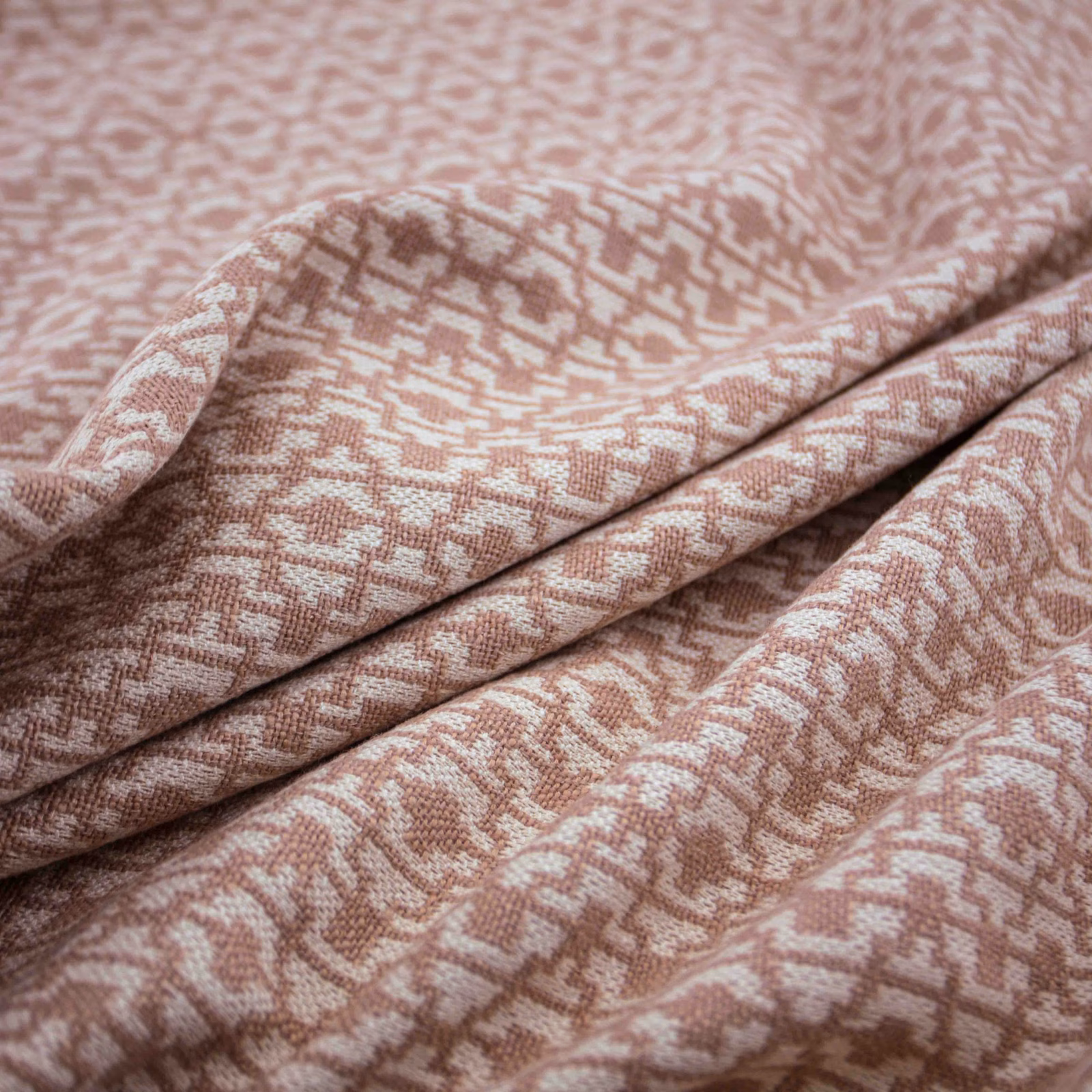Folded muted blush-pink fabric with a small broken geometric woven motif