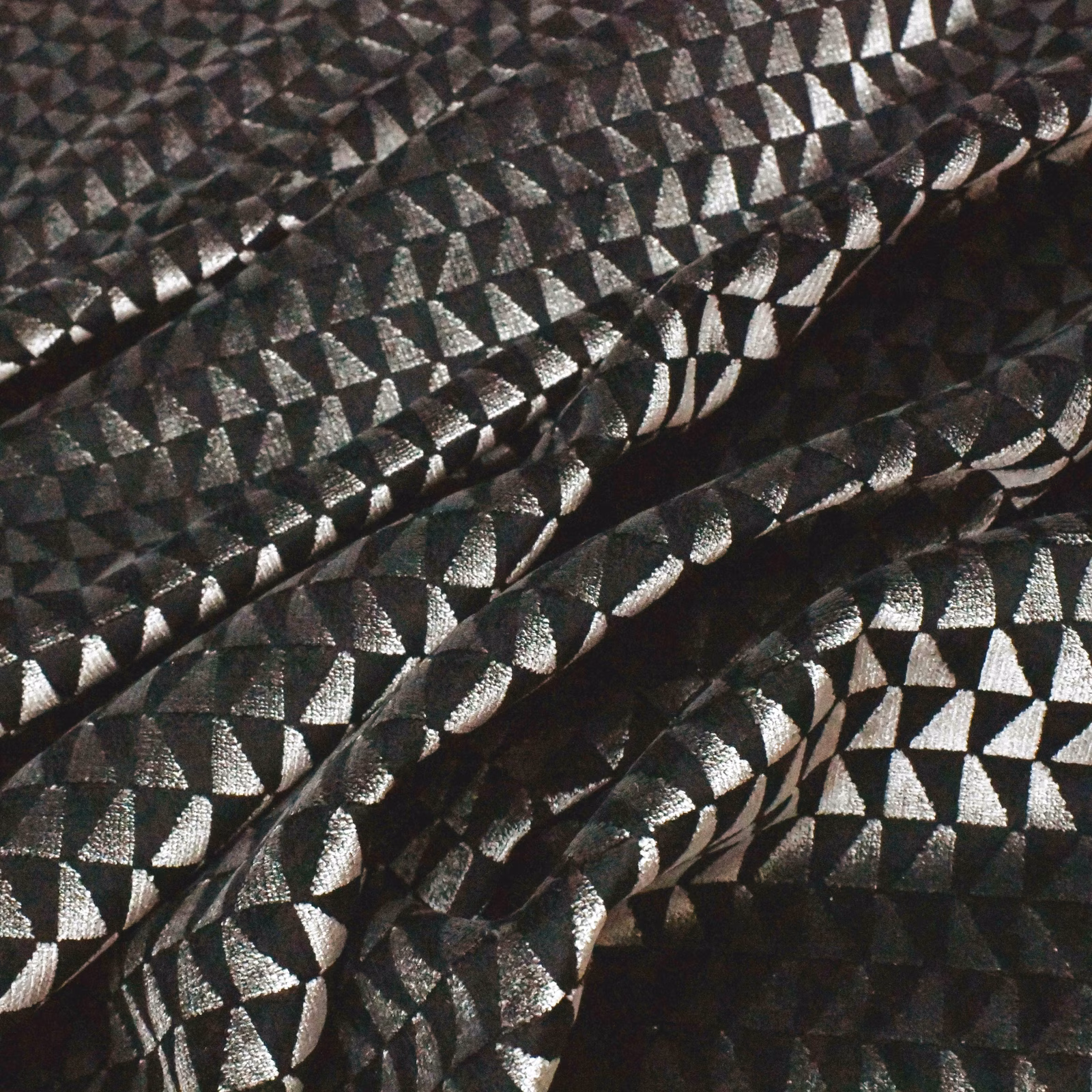 Black textile with silver geometric facets catching light across folded ridges