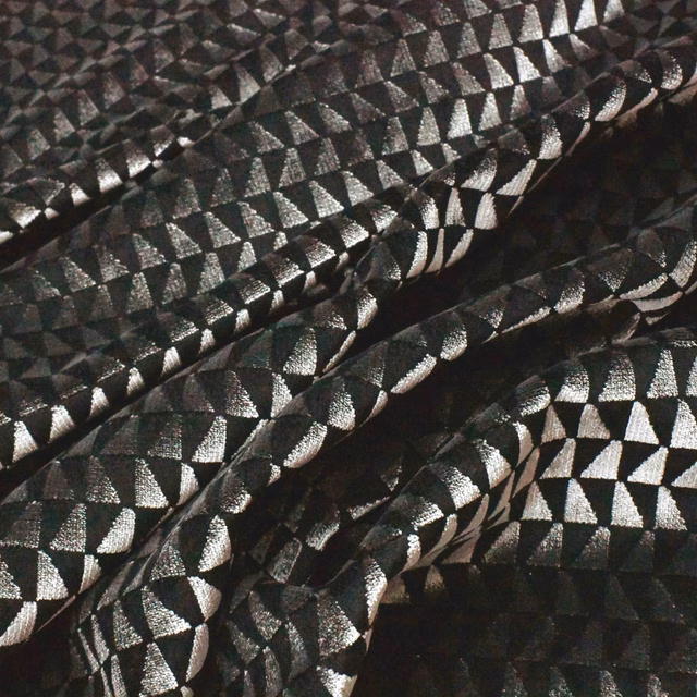 Black textile with silver geometric facets catching light across folded ridges