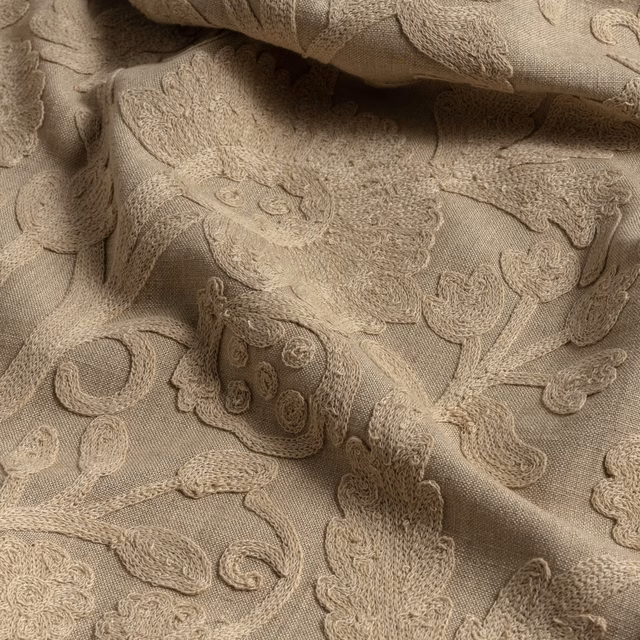 Warm flax-beige fabric with raised paisley, floral curls, and softly shadowed folds