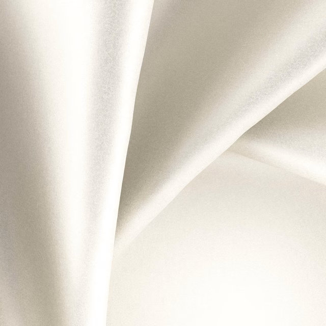 Pale ivory glossy fabric falling in broad, softly shadowed draped folds