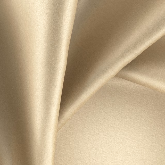 Warm brass-gold fabric with smooth satin sheen folded into fluid sculptural drapes