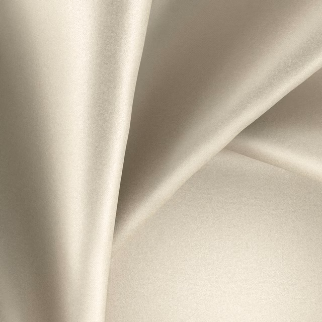 Pale warm ivory Glossy Luna fabric falling in smooth, lustrous folds
