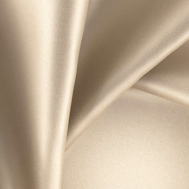 Warm champagne-beige glossy fabric draped in softly reflective folds
