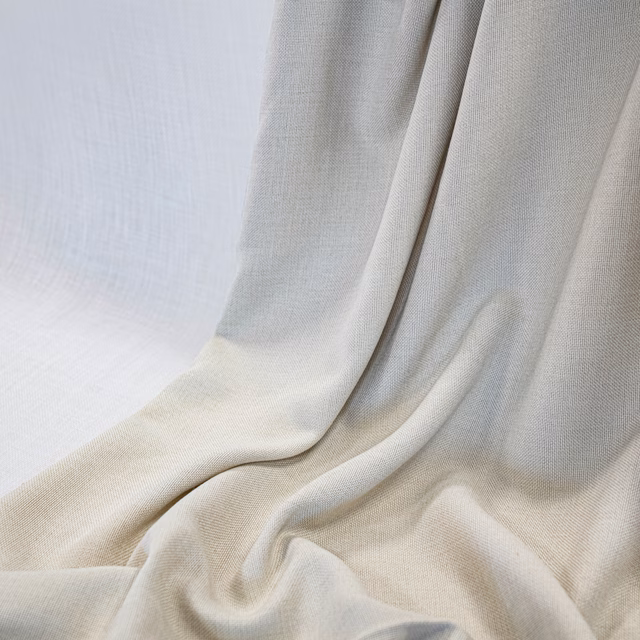 Warm ivory fabric draped in fluid folds, showing a fine woven texture and soft shadows
