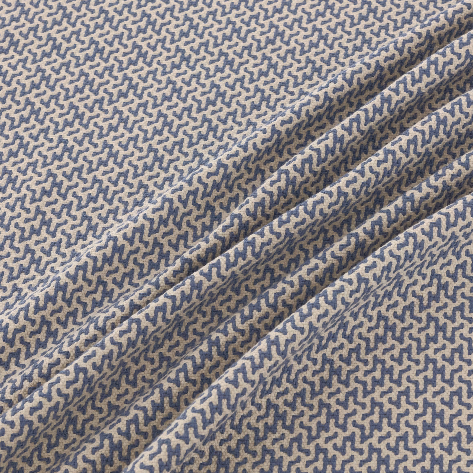 Blue-grey meandering motif on taupe woven fabric, shown folded in close-up