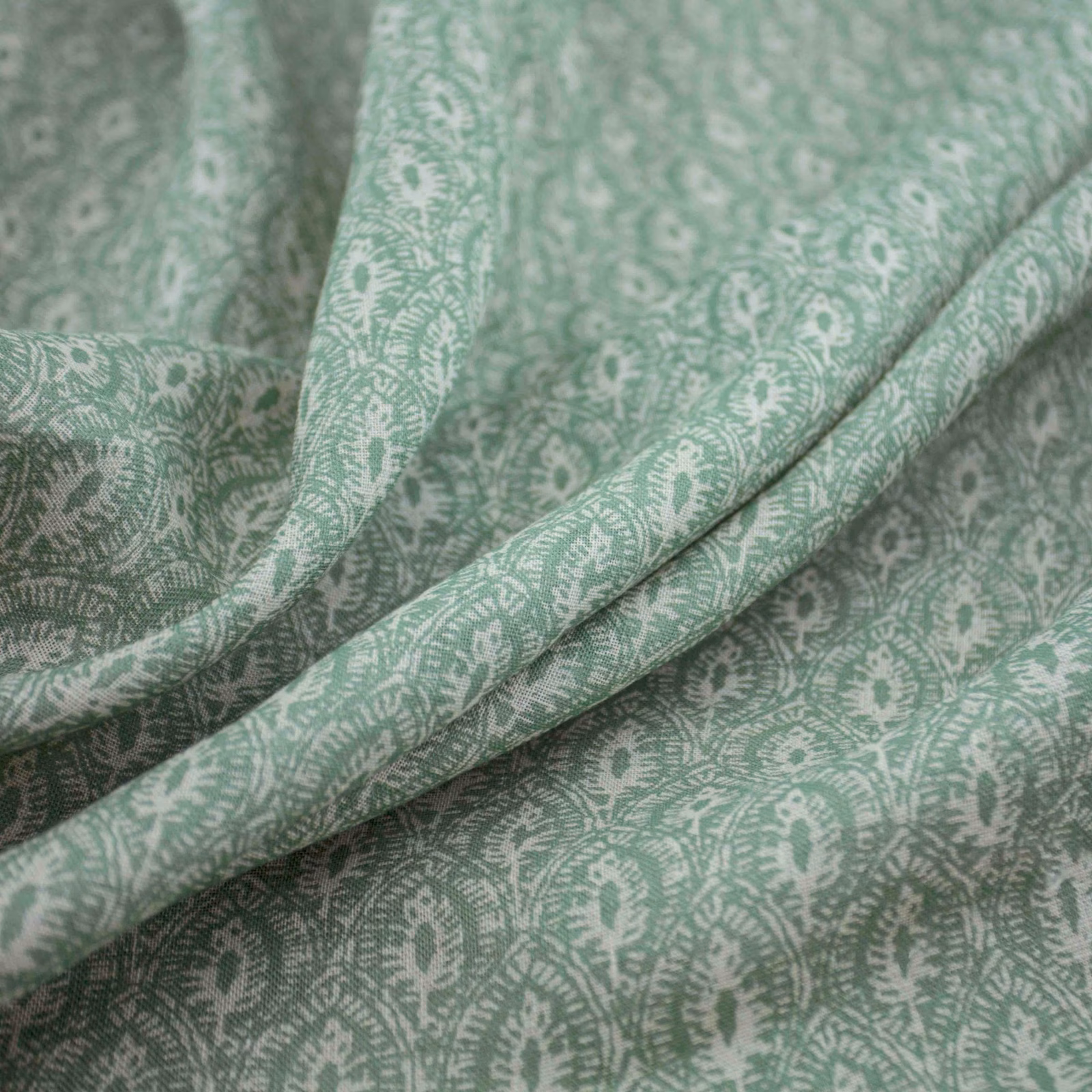 Soft celadon fabric with pale paisley motifs and fluid folded texture