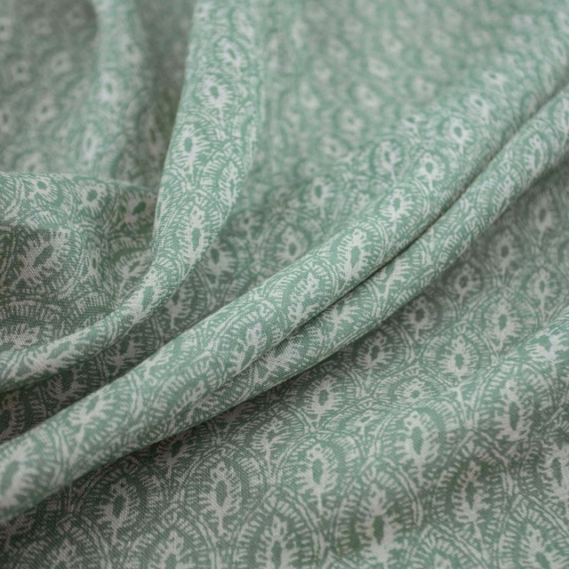 Soft celadon fabric with pale paisley motifs and fluid folded texture