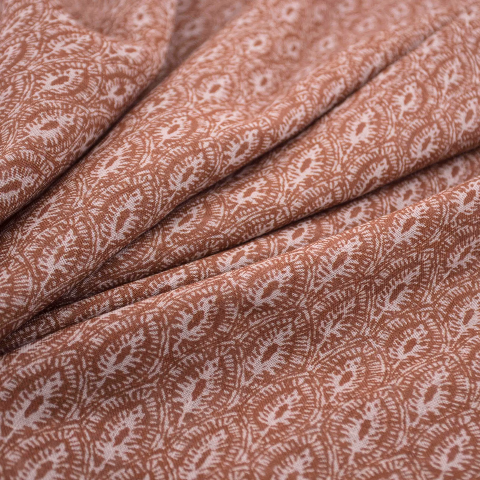 Folded henna-rose fabric with cream paisley foliage motifs and a softly textured surface