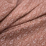 Folded henna-rose fabric with cream paisley foliage motifs and a softly textured surface