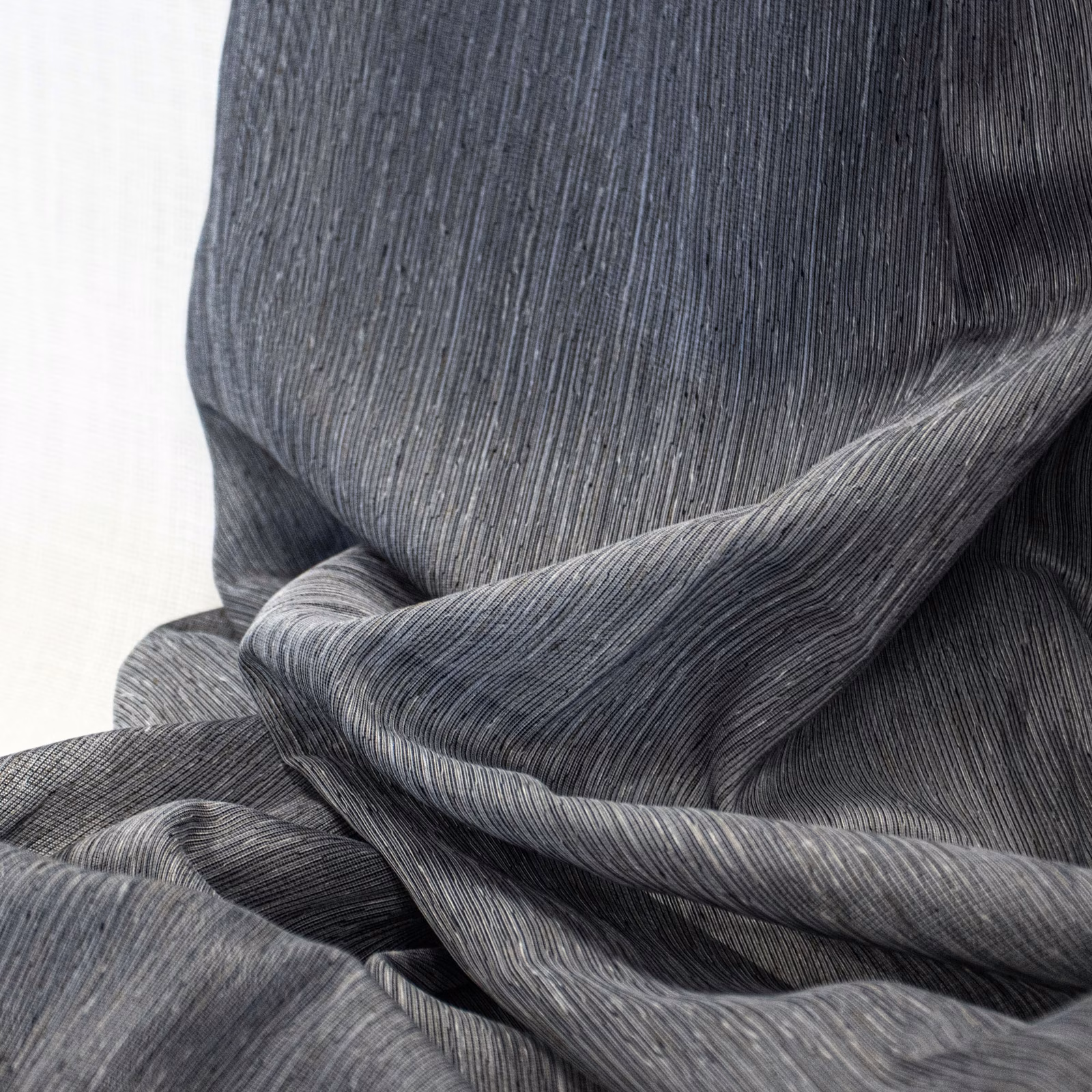 Charcoal-grey textile with fine vertical striations gathered into fluid rippling folds