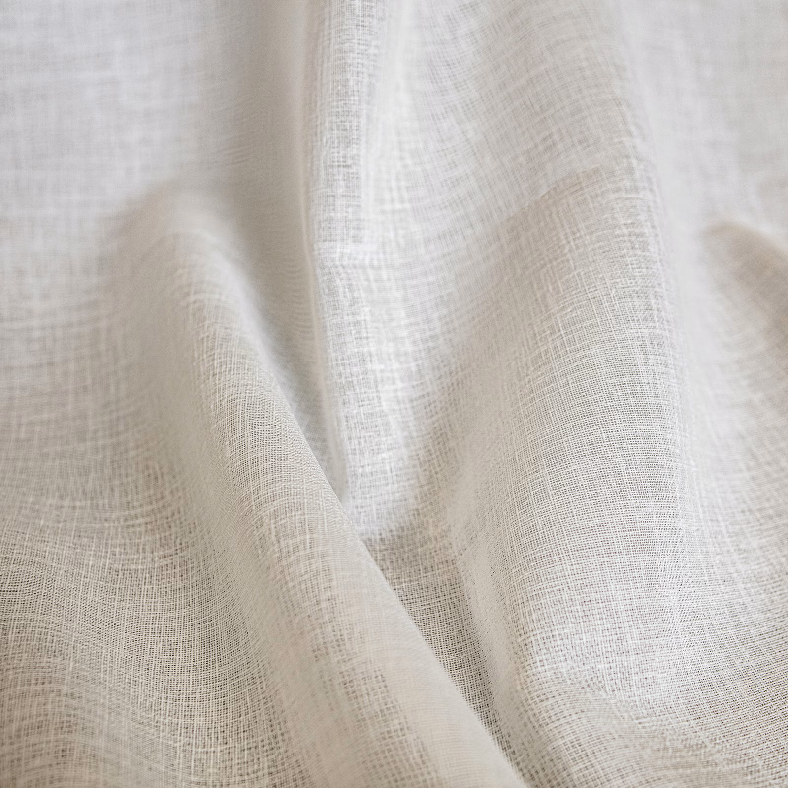 Pale ivory cream fabric with a fine open crosshatched weave folded into soft drapery pleats